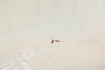 Aerial drone shot of woman lying in water on white sand beach and enjoying vacations. Tropical travel concept.
