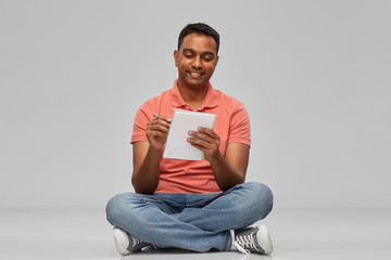 emotion, expression and people concept - smiling indian man in polo shirt writing to notebook over gray background