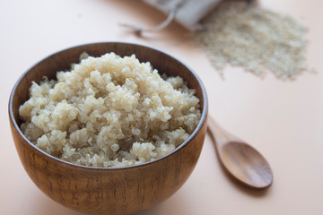  cooked quinoa in bowl and wooden spoon on brown background
