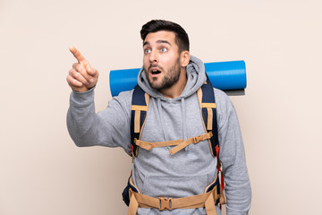 Young mountaineer man with a big backpack over isolated background pointing away