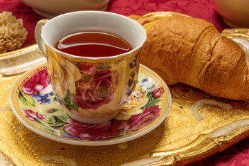Tea time in vintage granny style. Floral chine cup of black tea and French simple croissant on background 