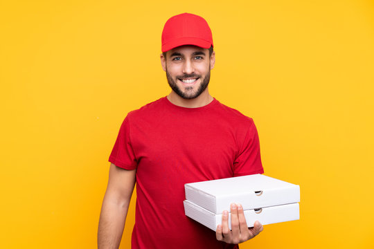 pizza delivery man with work uniform picking up pizza boxes over isolated yellow background smiling a lot