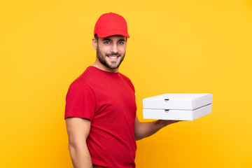 pizza delivery man with work uniform picking up pizza boxes over isolated yellow background smiling...