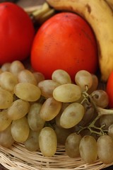 Persimmons bananas and grapes in a wooden basket 