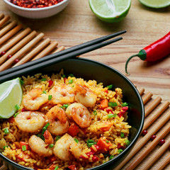 Classic Shrimp Fried Rice with fresh shrimp, rice, green onions, vegetables and lime in a bowl. Healthy Thai food on a wooden table.