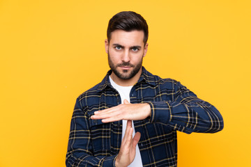 Young handsome man with beard over isolated yellow background making time out gesture
