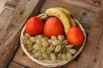 Persimmons bananas and grapes in a wooden basket 