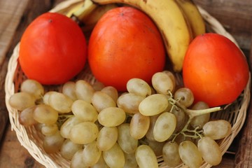 Persimmons bananas and grapes in a wooden basket 