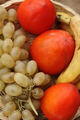 Persimmons bananas and grapes in a wooden basket 