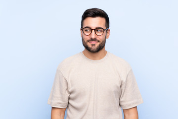 Fototapeta premium Young handsome man with beard over isolated blue background standing and looking to the side