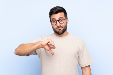 Young handsome man with beard over isolated blue background showing thumb down sign © luismolinero