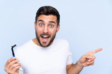 Young handsome man shaving his beard over isolated background surprised and pointing finger to the side