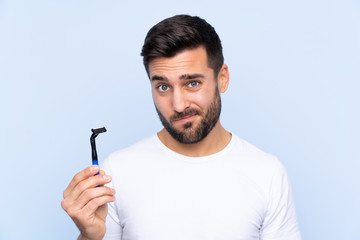 Young handsome man shaving his beard over isolated background with sad expression