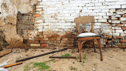 Old wooden chair standing near the brick wall of a ruined house.
