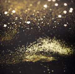 Beautiful Christmas light background. Abstract glitter bokeh and scattered sparkles in gold, on black