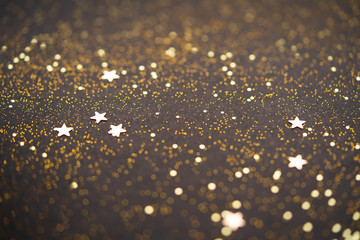 Beautiful Christmas light background. Abstract glitter bokeh and scattered sparkles in gold, on black