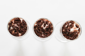 Layered trifle dessert with chocolate sponge cake, whipped cream and fruit jelly in serving glasses. - Image