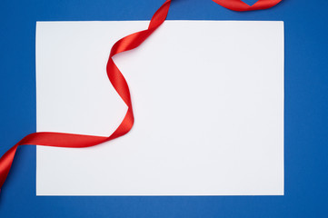 empty white sheet of paper and red silk twisted ribbon on a blue background