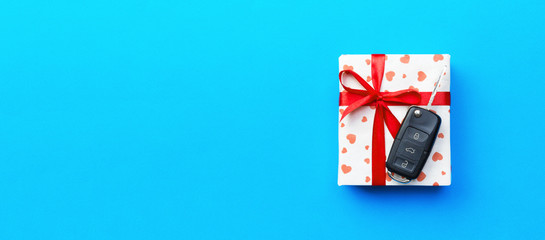 Give gift car key concept top view. Present box with red ribbon bow, heart and car key on blue colored background