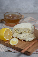 Sliced ​​homemade cheese with lemon and honey in a rustic style on a gray stone background