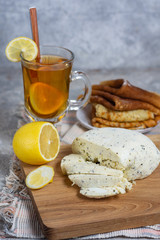 Lemon tea in a glass mug with lemon and a spoon with sliced ​​cottage cheese, honey and pancakes in a rustic style on a gray stone background vertical arrangement