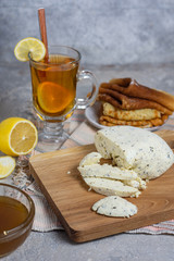 Lemon tea in a glass mug with lemon and a spoon with sliced ​​cottage cheese, honey and pancakes in a rustic style on a gray stone background vertical arrangement