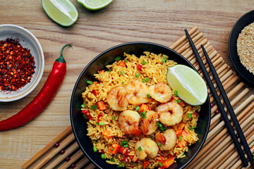 Classic Shrimp Fried Rice with fresh shrimp, rice, green onions, vegetables and lime in a bowl. Healthy Thai food on a wooden table. Top view, directly above shot.