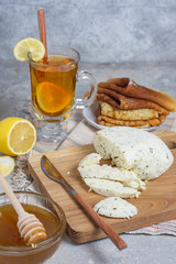 Lemon tea in a glass mug with lemon and a spoon with sliced ​​cottage cheese, honey and pancakes in a rustic style on a gray stone background vertical arrangement