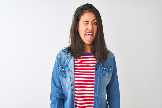 Young chinese woman wearing striped t-shirt and denim shirt over isolated white background sticking tongue out happy with funny expression. Emotion concept.