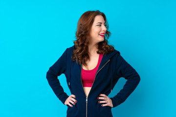 Young sport woman over isolated blue background posing with arms at hip and looking side