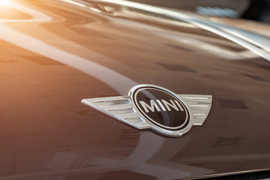 Designer metal shiny brand logo close-up on a polished, light-reflecting hood as a symbol of the manufacturer of expensive brown cars model mini cooper countryman.