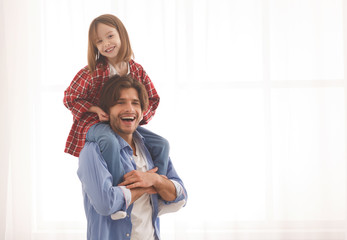 Joyful little girl sitting on her daddy shoulders