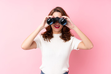 Young Russian woman over isolated pink background with black binoculars