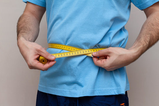 man in a blue T-shirt measures the waist with a yellow tape