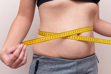 woman measures the waist with a yellow tape. Diet fitness concept.