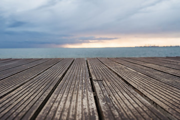 Fototapeta na wymiar View of wooden decking, sea and gray sky at dusk.