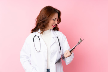 Young Russian woman over isolated pink background with doctor gown and holding a folder