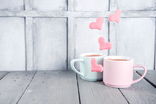 Two pastel cups with hot cocoa drink or latte coffee with flying red and pink hearts levitation marshmallows. Valentine's day greetings background. Love winter holidays cute picture.