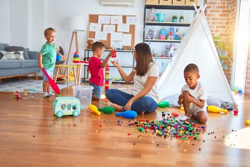 Young beautiful teacher and toddlers playing around lots of toys at kindergarten