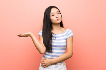Teenager asian girl over isolated pink background unhappy for not understand something