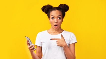 Portrait of shocked black teen pointing at mobile phone