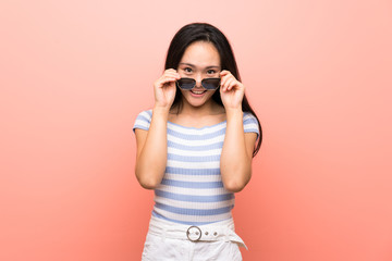 Teenager asian girl over isolated pink background with glasses and surprised