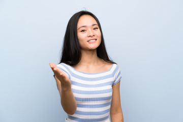 Teenager asian girl over isolated blue background handshaking after good deal