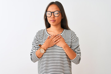 Young chinese woman wearing striped t-shirt and glasses over isolated white background smiling with hands on chest with closed eyes and grateful gesture on face. Health concept.