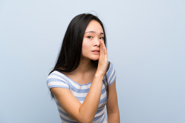 Teenager asian girl over isolated blue background whispering something