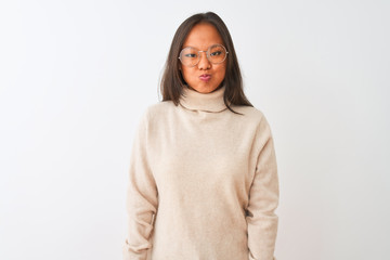 Fototapeta premium Young chinese woman wearing turtleneck sweater and glasses over isolated white background puffing cheeks with funny face. Mouth inflated with air, crazy expression.