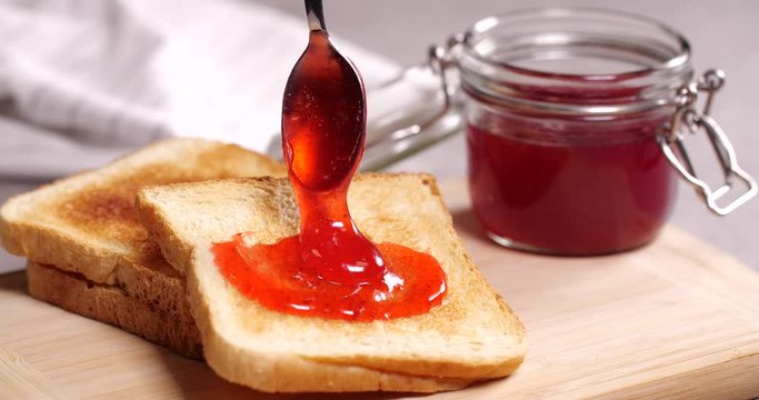 Woman spreading delicious strawberry jam onto crispy toast, closeup