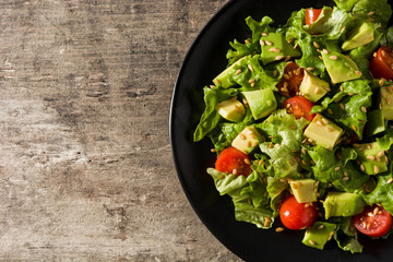 Salad with avocado, lettuce, tomato, seeds on wooden table. Top view copy space