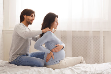 Caring husband massaging shoulders of his pregnant wife