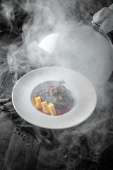 Gorgeous serve of beef with potatoes and vegetable stew in the smoke. Restaurant menu. Background black boards.